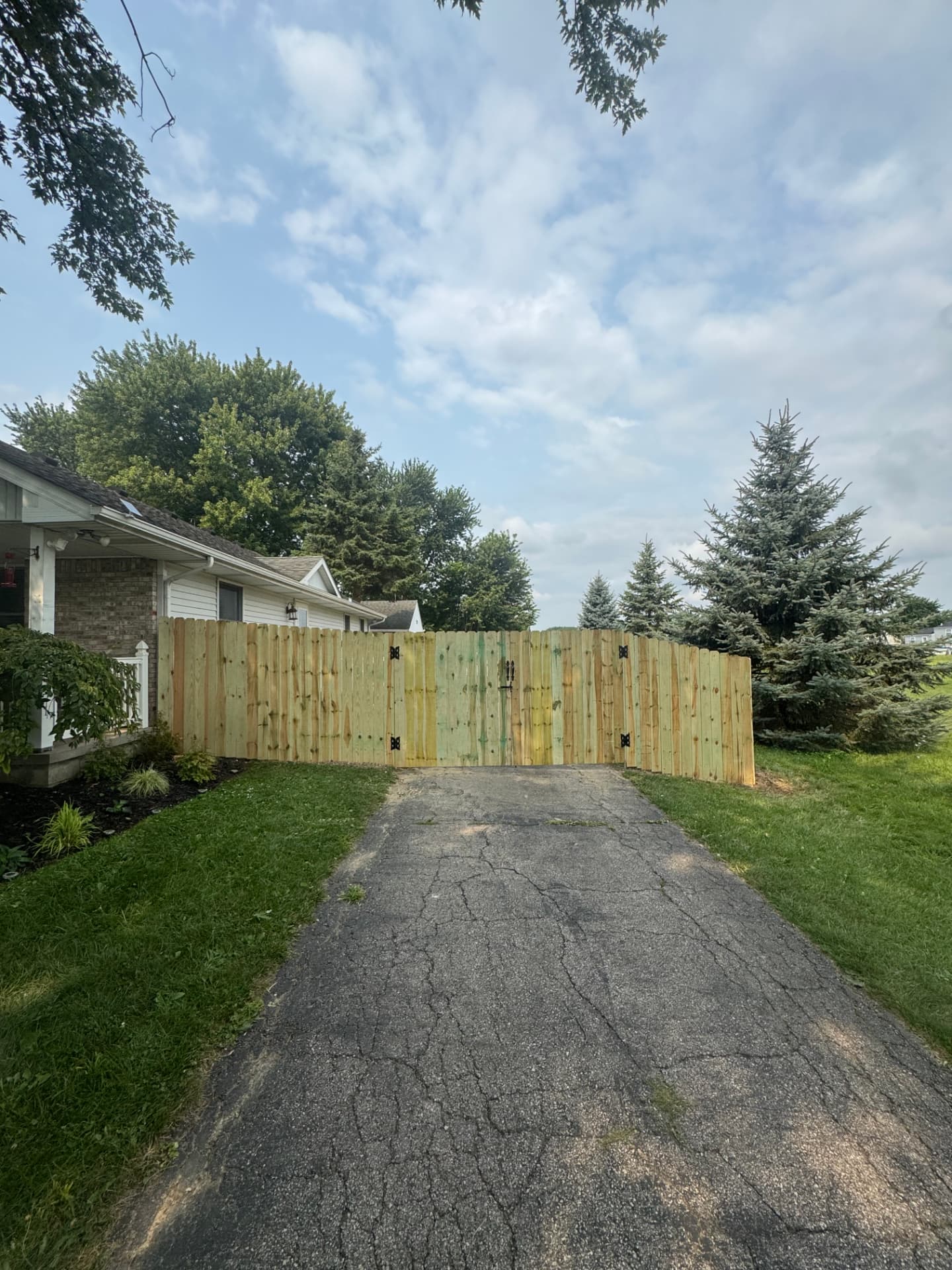 New pressure-treated privacy fence with a wide double drive gate across an asphalt driveway