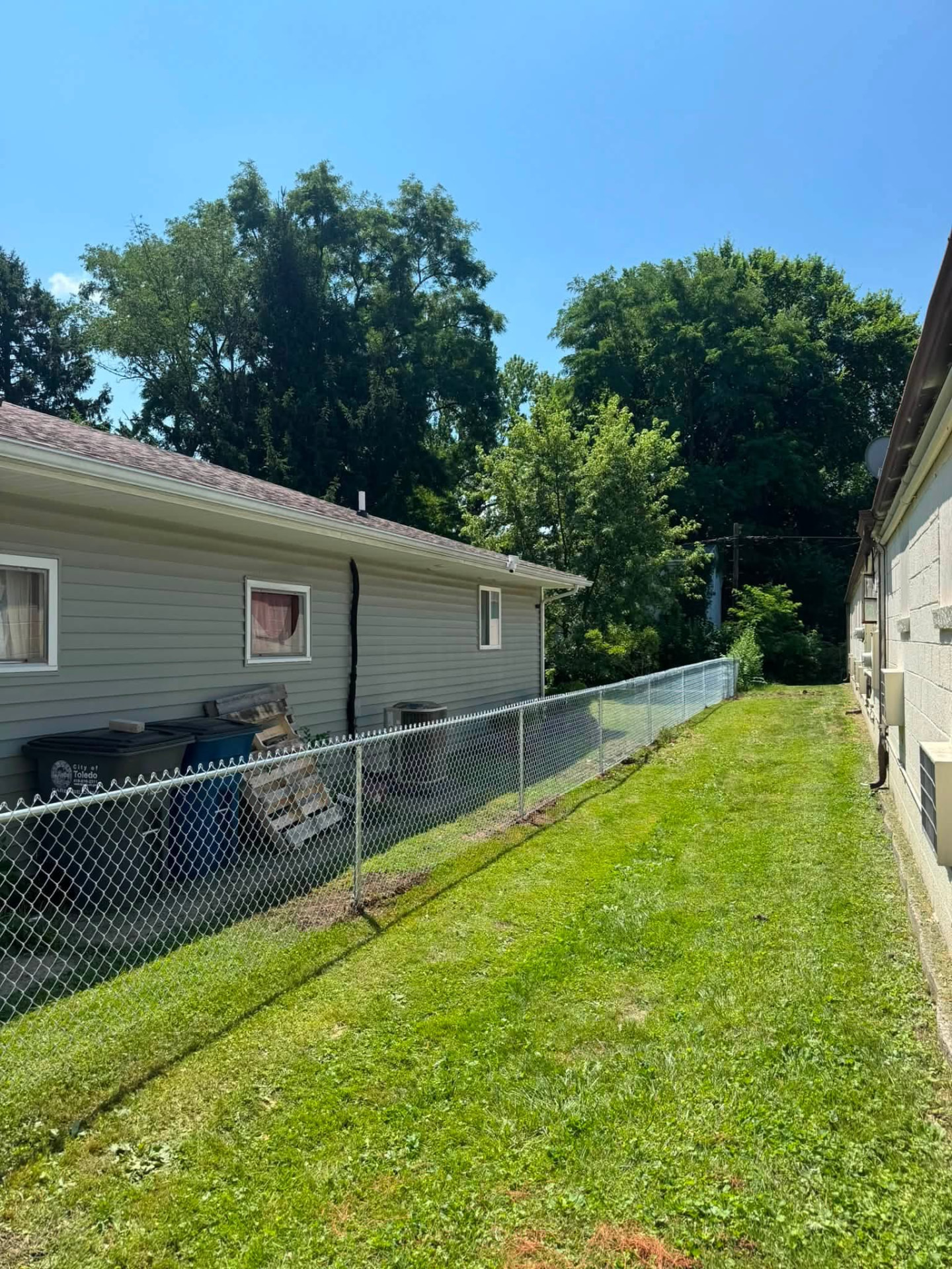 New galvanized chain-link fence running along a side yard between two homes in Toledo, Ohio