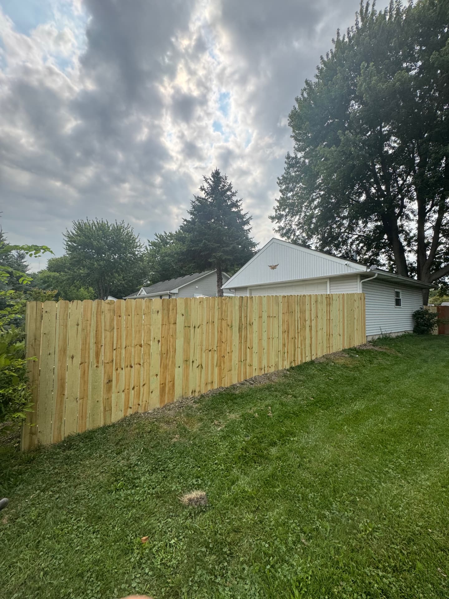 New dog-ear privacy fence running along a sloped back yard beside a detached garage
