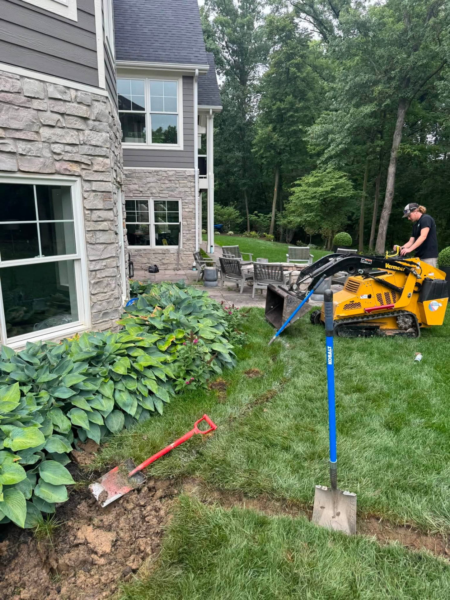HPC operator running a compact track loader to regrade a landscape bed beside a home