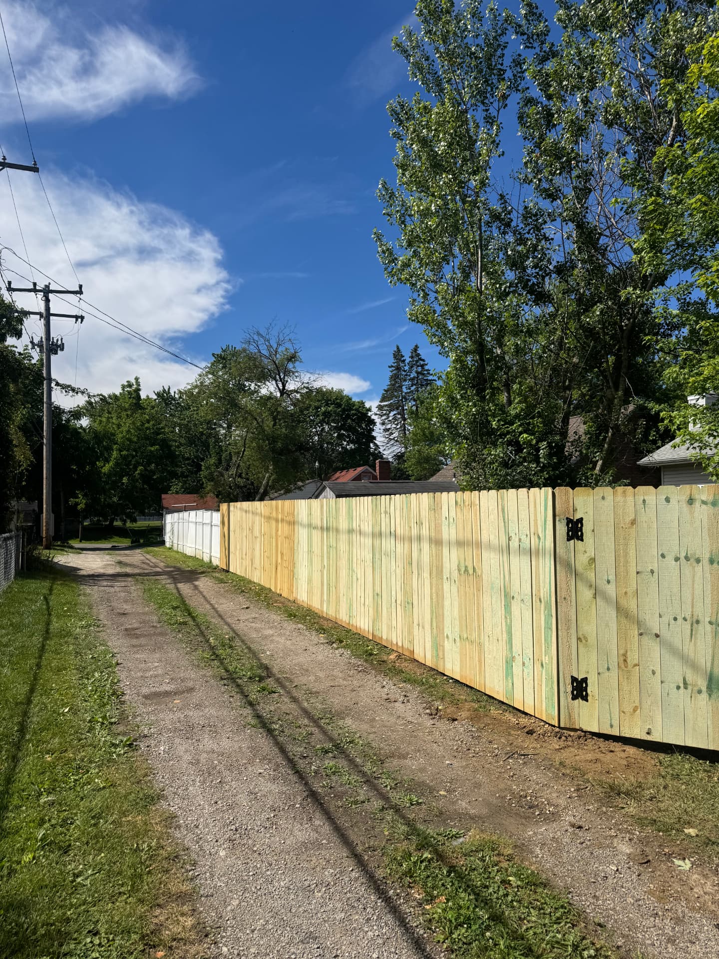 Long run of new wood privacy fence with a double gate along a gravel alley